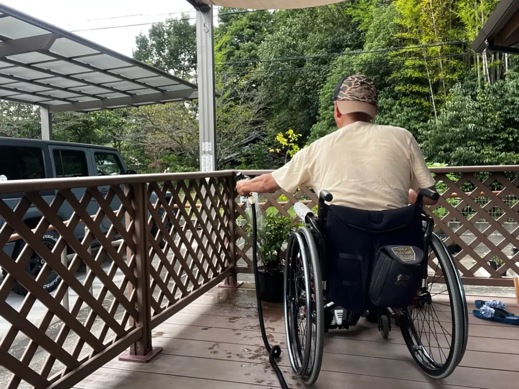車椅子から伸縮ホースでウッドデッキの植物へ水やりをする様子
