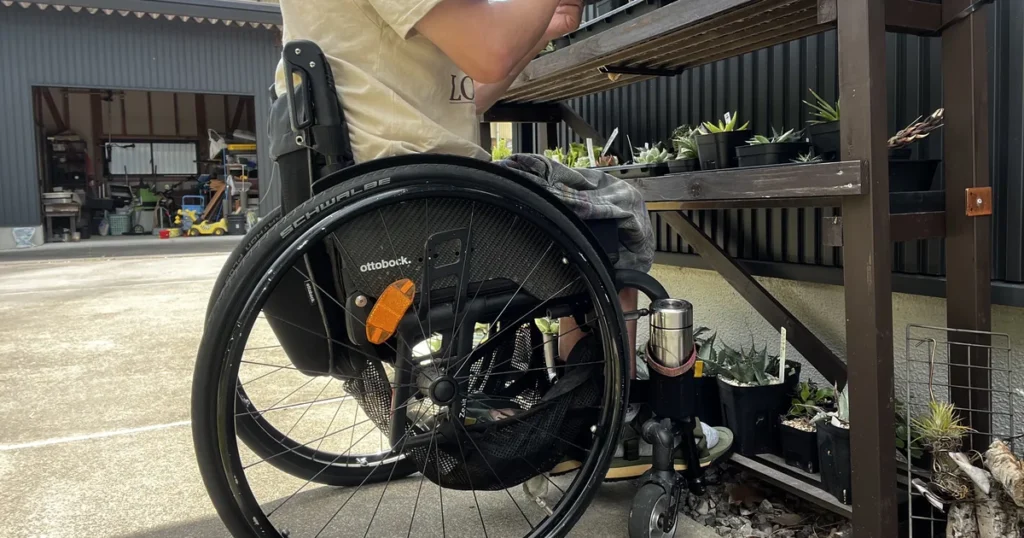 車椅子に座って屋外の植物棚を手入れしている様子