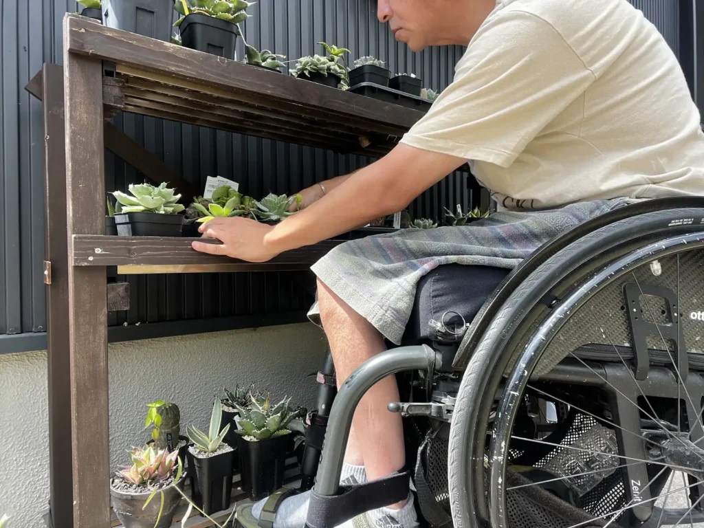 車椅子から植物棚の鉢を並べ直している様子